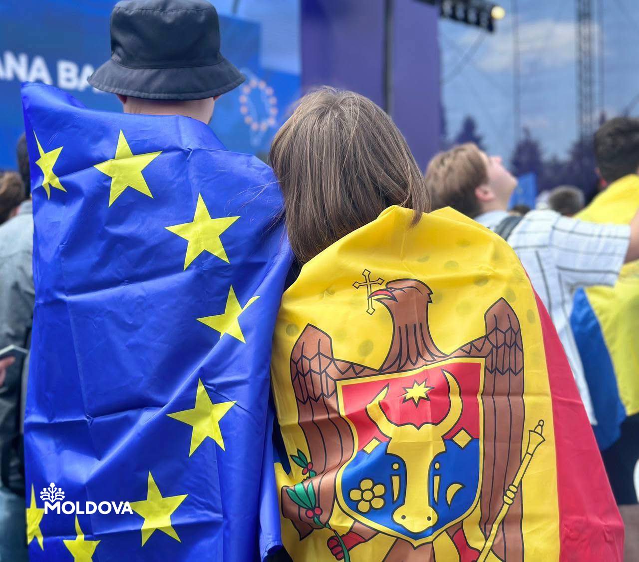 Two people seen from behind, one wrapped in the flag of the European Union, one in the flag of the Republic of Moldova